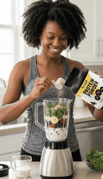 A woman adding chocolate protein powder to a blender with healthy ingredients, making a delicious high-protein smoothie.