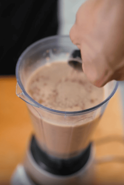 A person putting a scoop of EliteCore Protein with BCAAs to create a delicious chocolate protein smoothie.