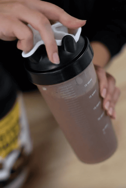 A person making a chocolate protein shake with no added sugar using EliteCore Zero-Sugar Whey Protein Powder.